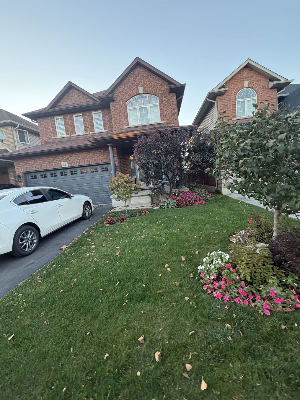 Green front lawn meeting a pink and white flower bed at a brick home in Hamilton