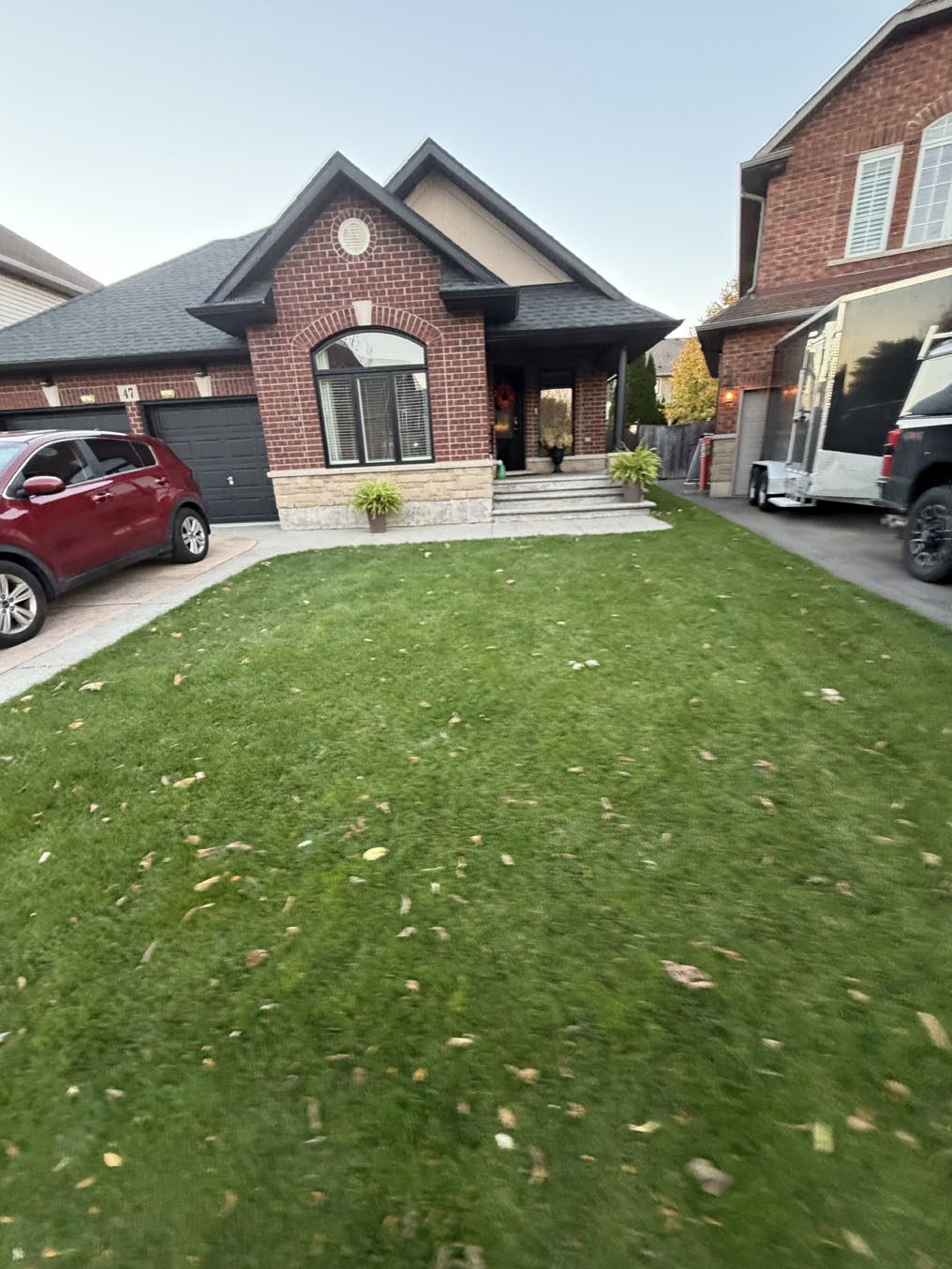 Clean, even sod lawn leading to a red-brick bungalow with an arched window in Hamilton