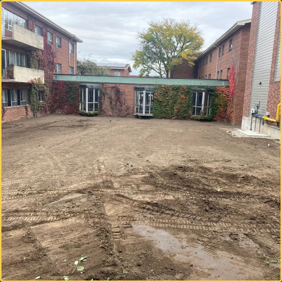 Professional soil grading and ground preparation in a brick apartment courtyard in Hamilton.