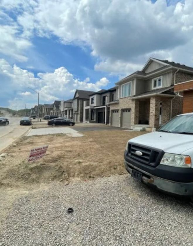 Commercial sod installation 4 A white landscaping truck parked in front of a row of newly built homes in a Hamilton subdivision, showing bare dirt front yards prepared for commercial standard pallet sod installation.