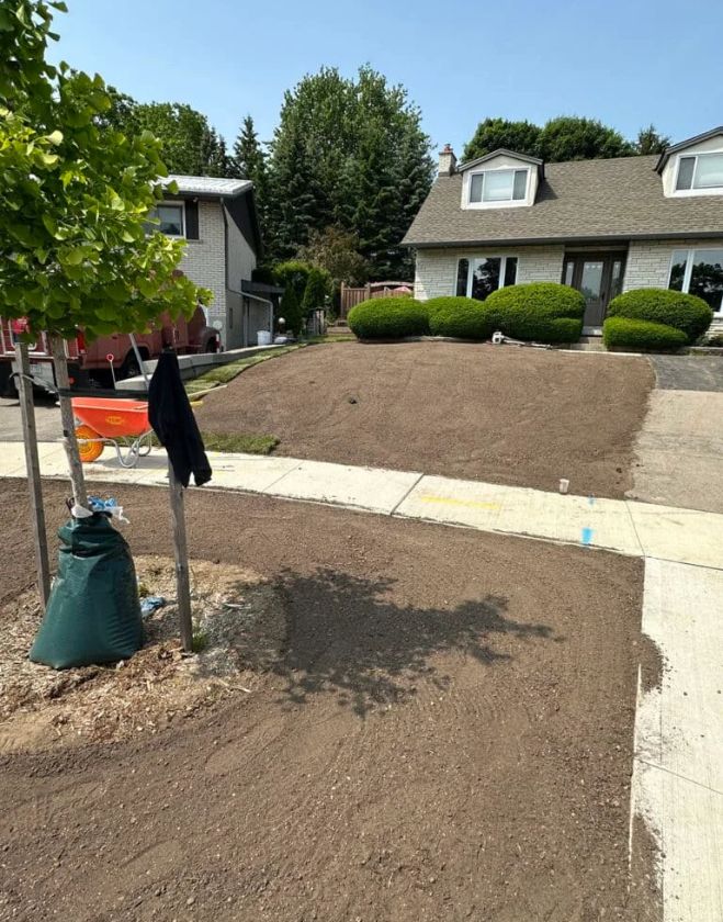 A residential front yard in Hamilton showing perfectly graded bare topsoil sloping down to a sidewalk, prepared for fresh sod installation.