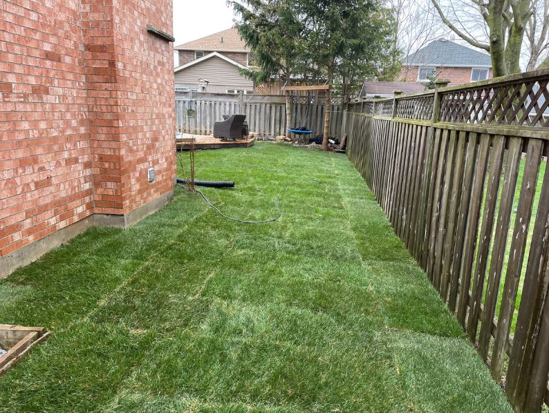 A homeowner standing in front of a brick house with a newly installed, perfectly graded sloped front lawn in Hamilton.