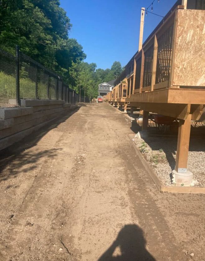 A long stretch of bare dirt behind residential townhouse decks in Hamilton, showing the excavation of dead grass caused by severe grub damage.