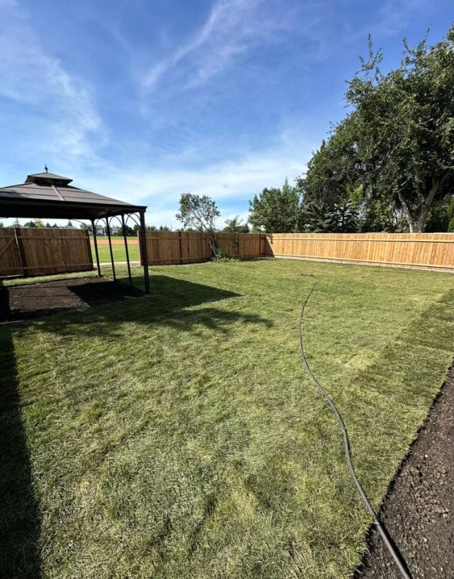 A wide view of a healthy, vibrant green backyard lawn with a wooden fence and a gazebo in Hamilton, representing the starting point for professional lawn fertilization and soil analysis.
