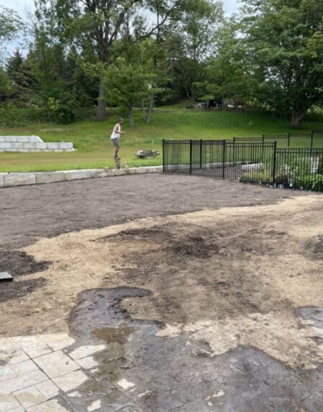 Lawn Repair 2 A bare, muddy residential backyard with exposed dirt being prepared for professional lawn repair and sod installation next to a black metal fence in Hamilton.