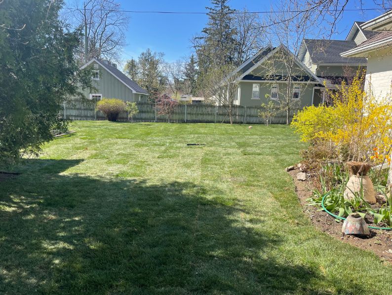 Newly laid sod in a narrow residential side yard between a brick house and a wooden fence, leading to a back deck in Hamilton.