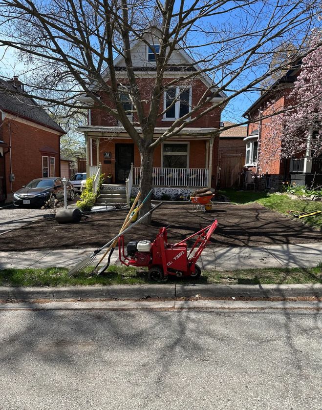 Gallery 3 A red sod cutter machine and landscaping rakes sitting on the curb in front of a freshly graded dirt yard prepared for new grass in Corktown, Hamilton.