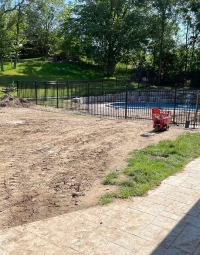 Lawn Repair 5 A Hamilton residential backyard showing leveled, graded topsoil ready for fresh sod installation, with a red landscaping machine parked near a black metal pool fence.